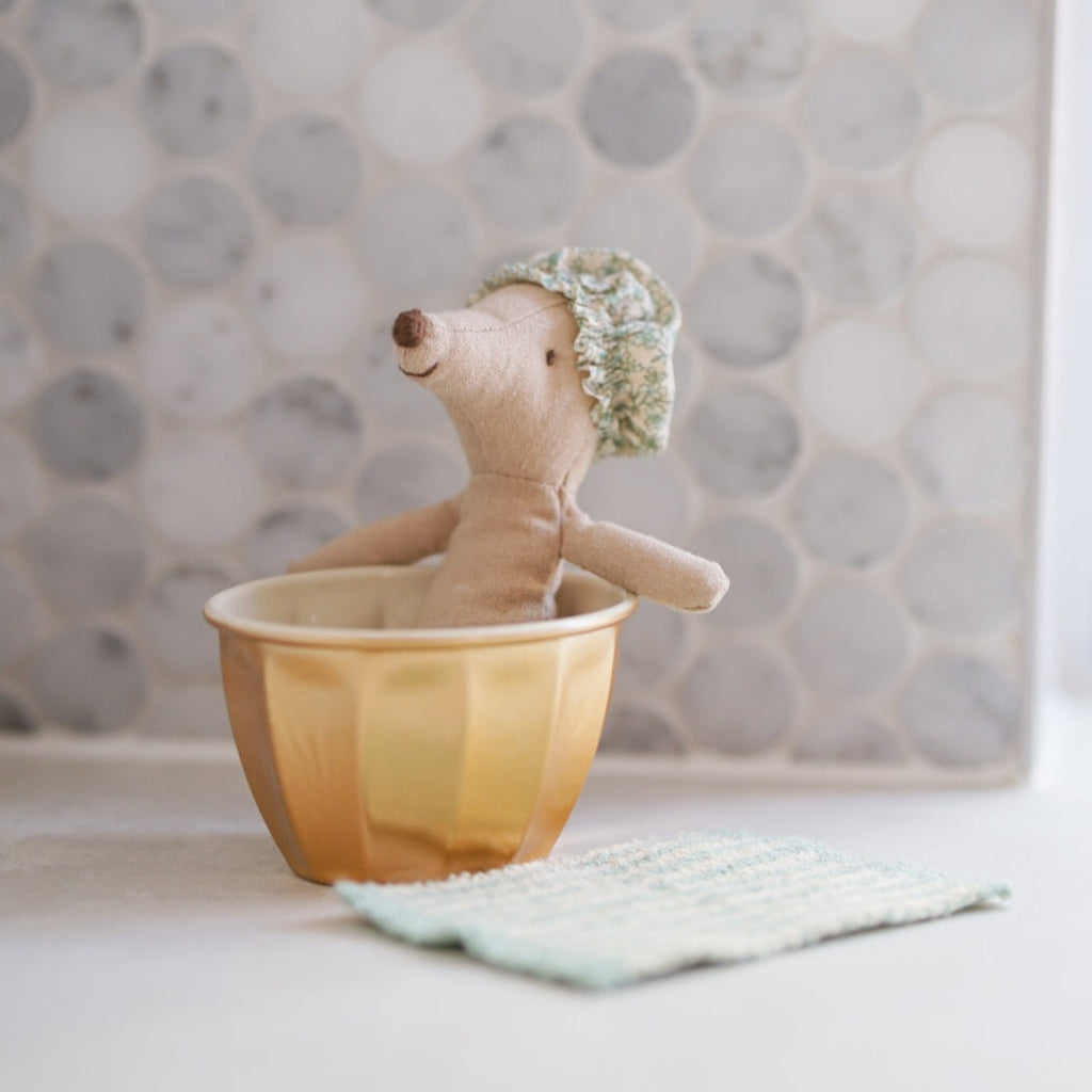 Wellness mouse sitting in bathtub with shower cap on and bath mat on floor