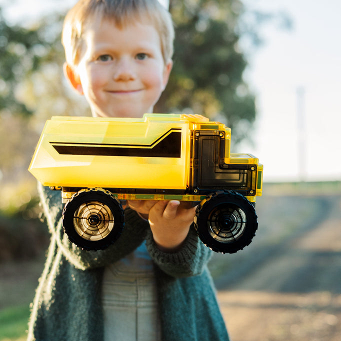 Child holding a yellow magnetic tile toy dump truck outdoors
