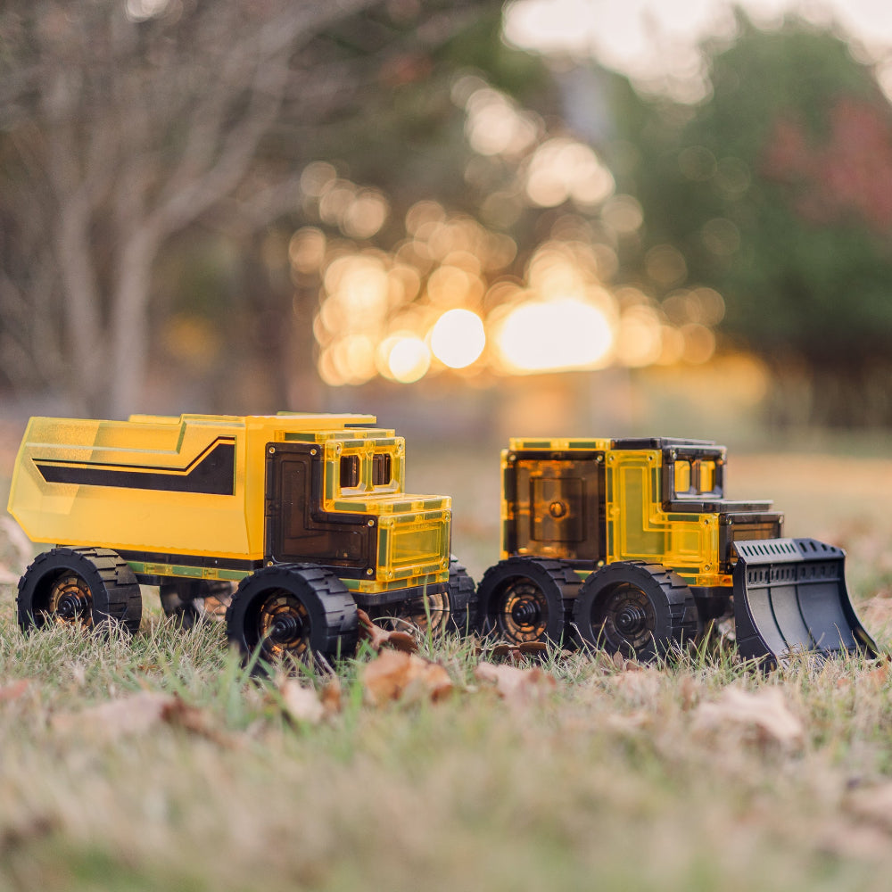 Two magnetic tile toy construction vehicles on grass with a blurred background