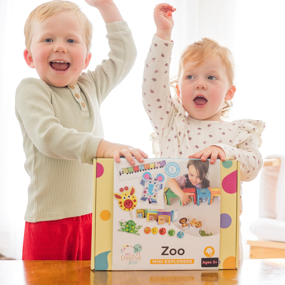 Children cheering holding up the mini explorer zoo craft box from My Creative Box with white curtain behind