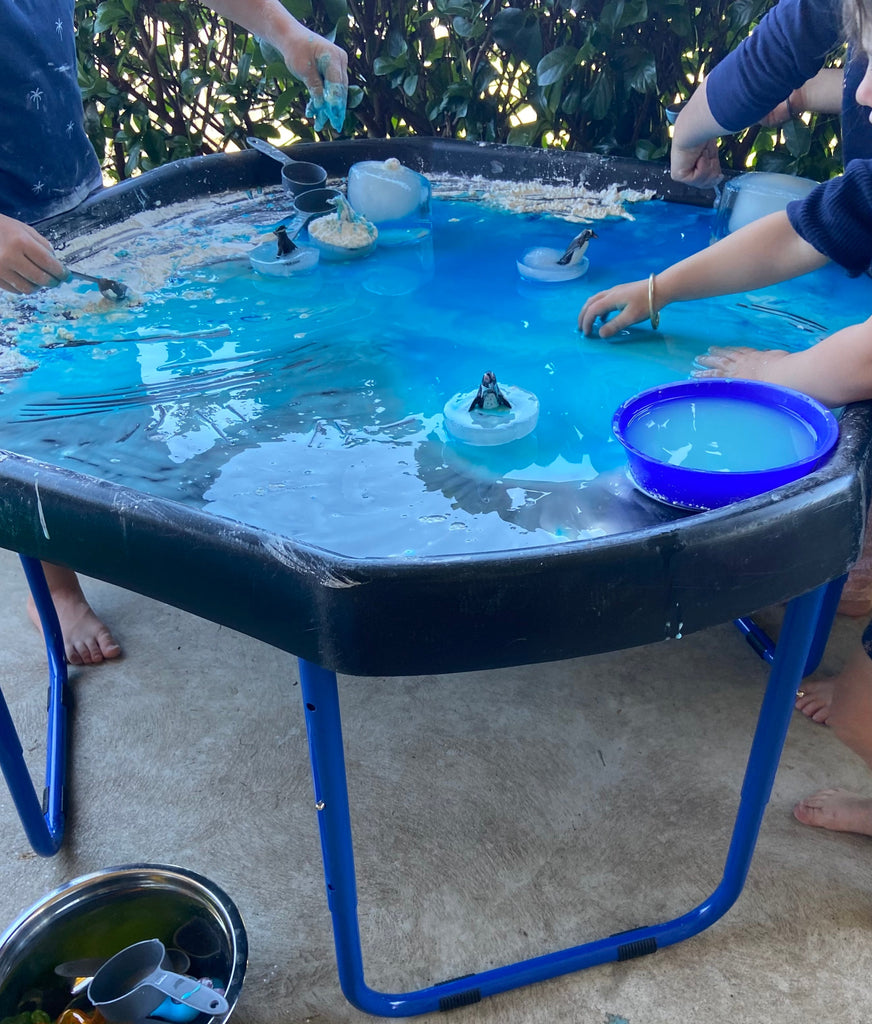 Tuff tray stand and tuff tray with flour, water and food colouring being used for messy play with 3 kids standing around stand