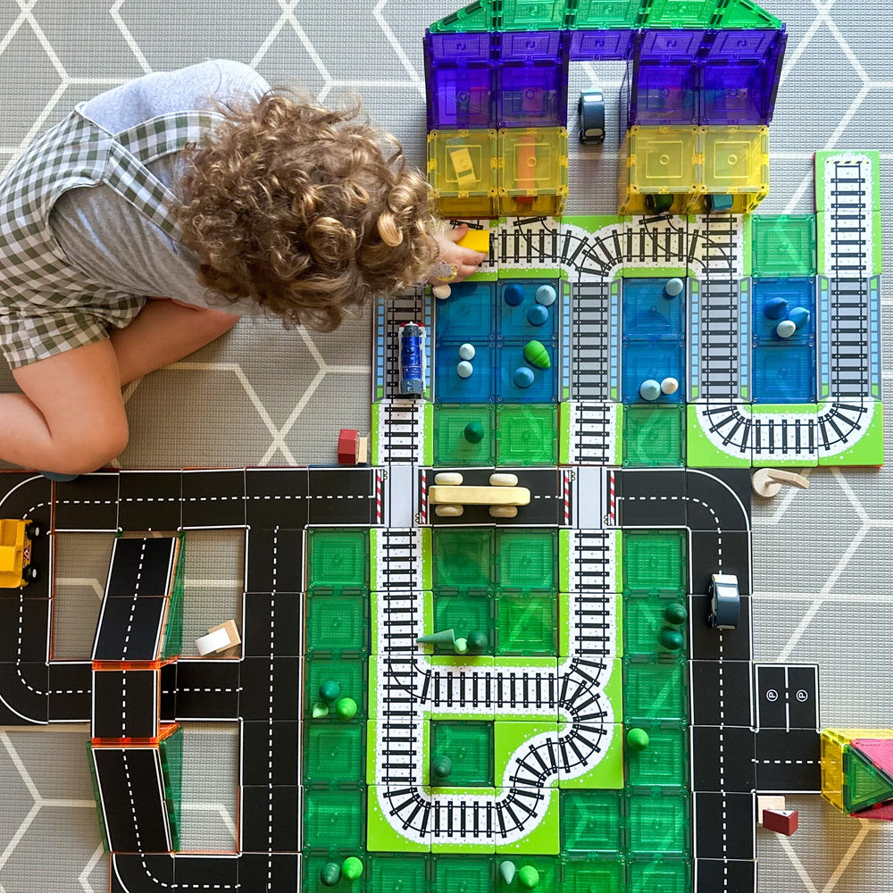 Child playing with train and road toppers that sit on magnetic tiles with train station made from learn and grow magnetic tiles