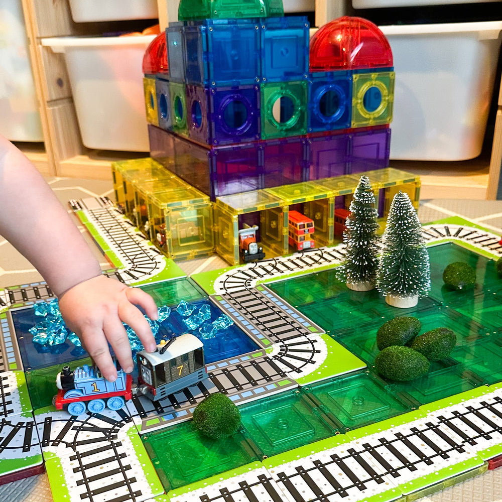 Child playing with thomas trains that are going along train toppers sitting on magnetic tiles