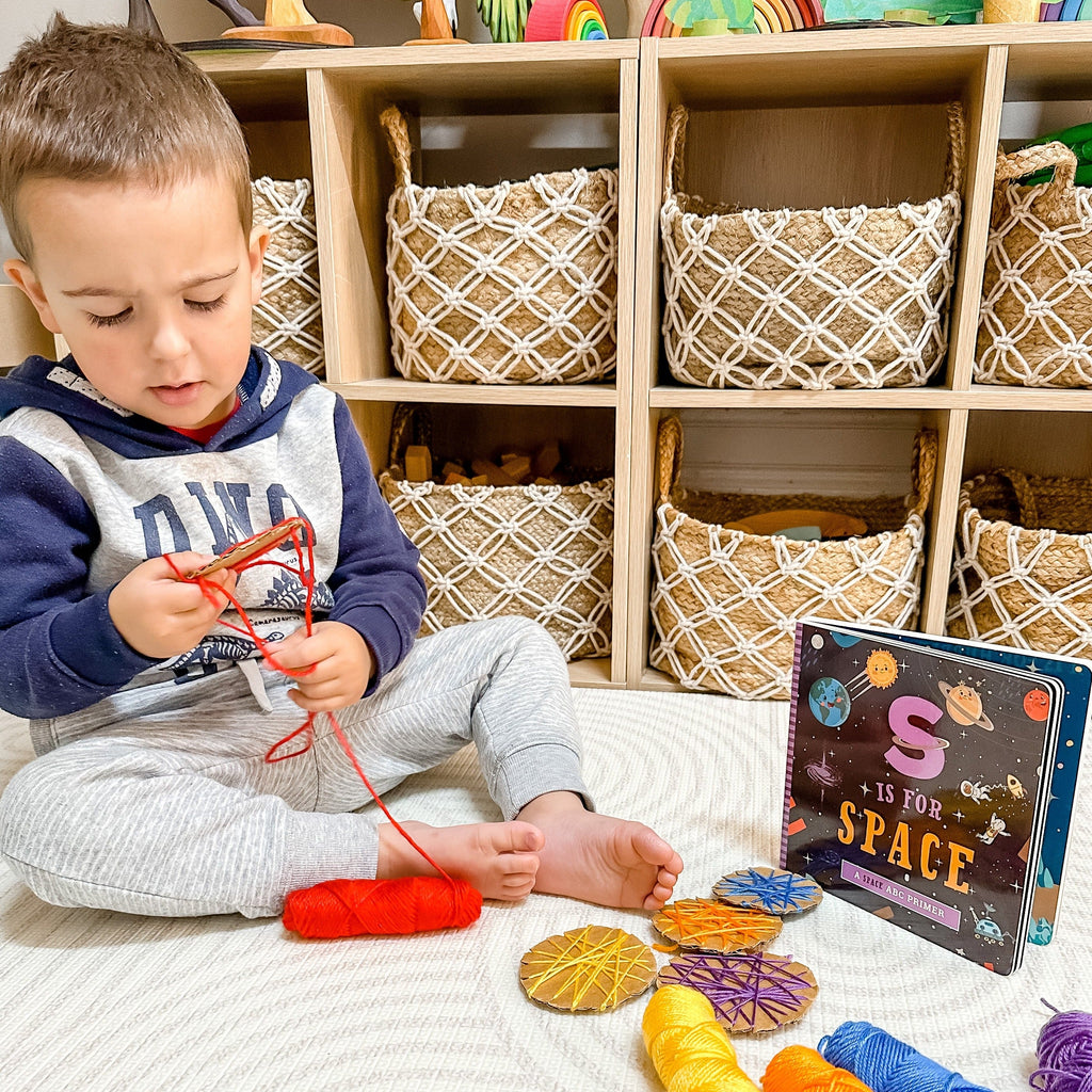 Child threading cardboard planets with S is for Space book in background of playroom