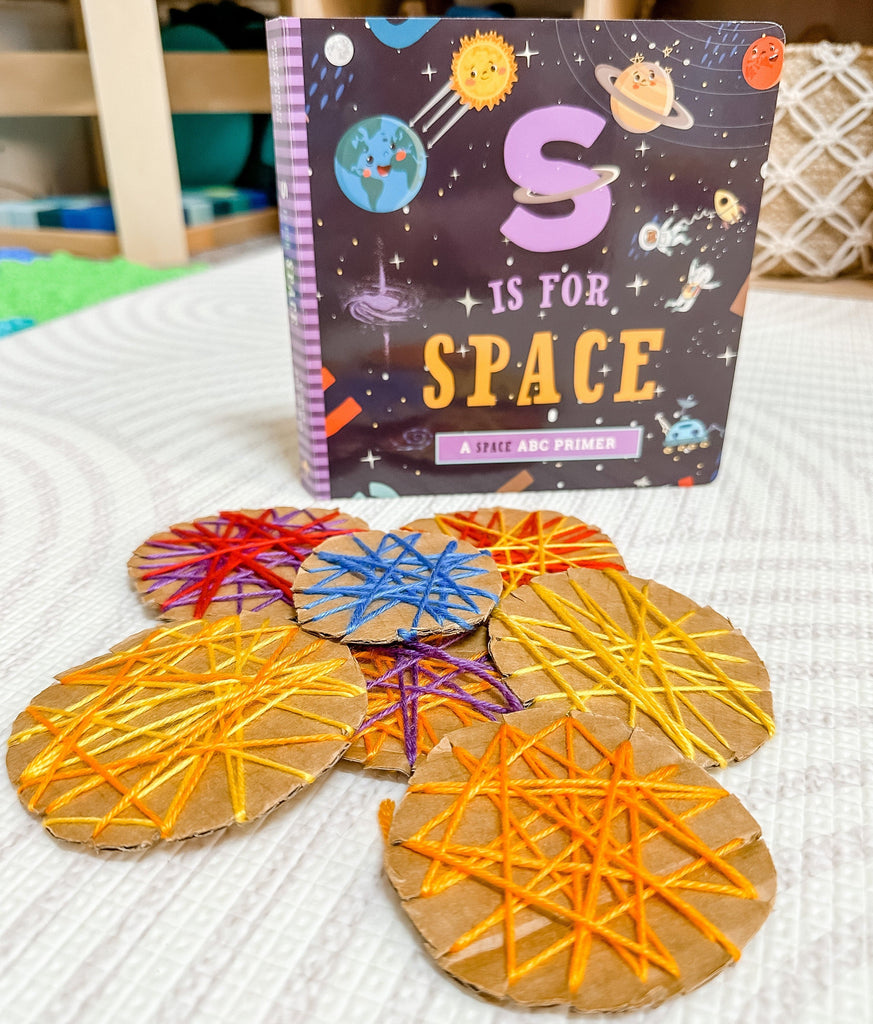 Threaded cardboard planets with S is for Space book in background of playroom