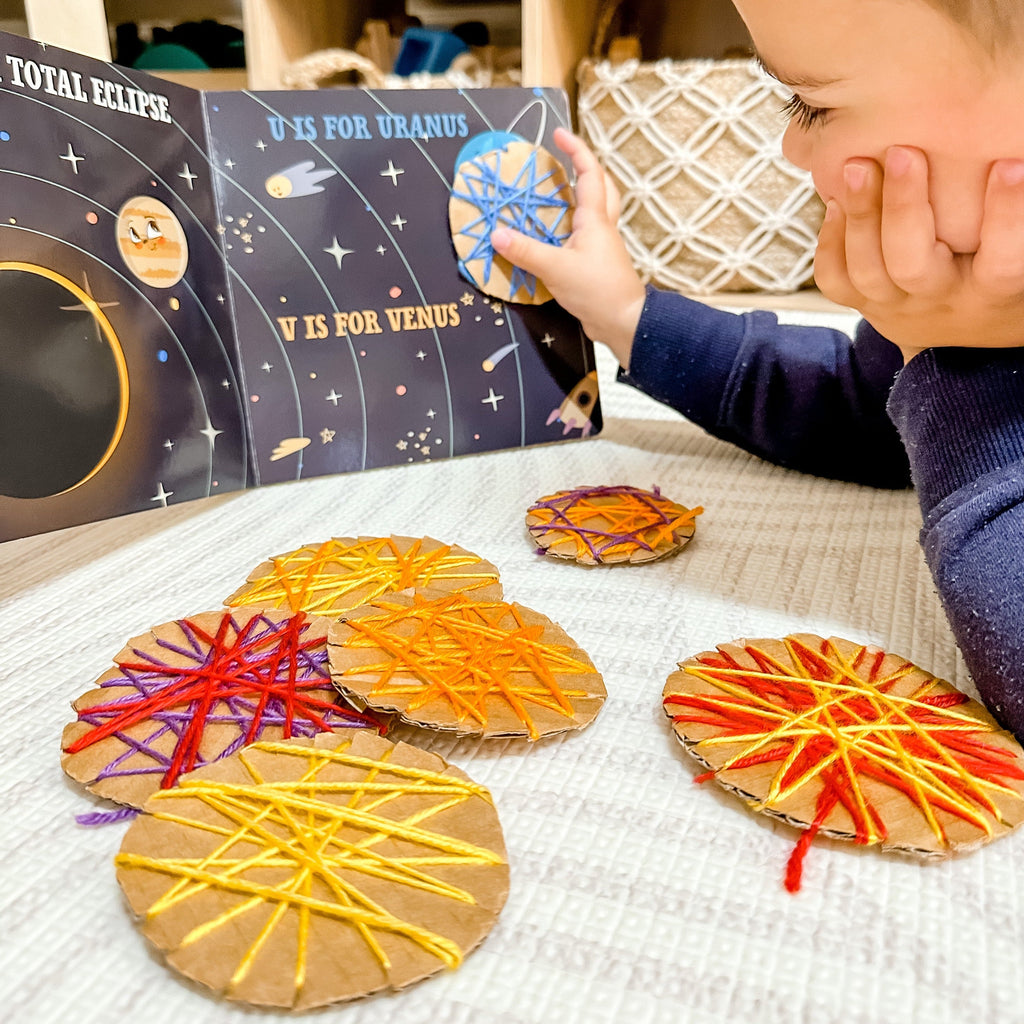 Child holding threading cardboard planets with S is for Space book 