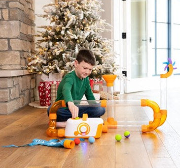 Child playing with a air toobz set on a wooden floor in a home setting with a Christmas tree.