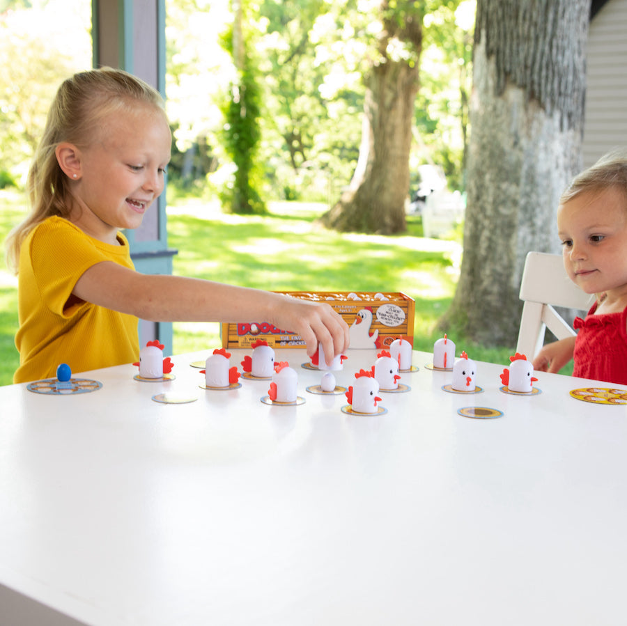 Children playing Fat Brain Toys Peek-A-Doodle Doo- chicken and egg game at a table with trees outside