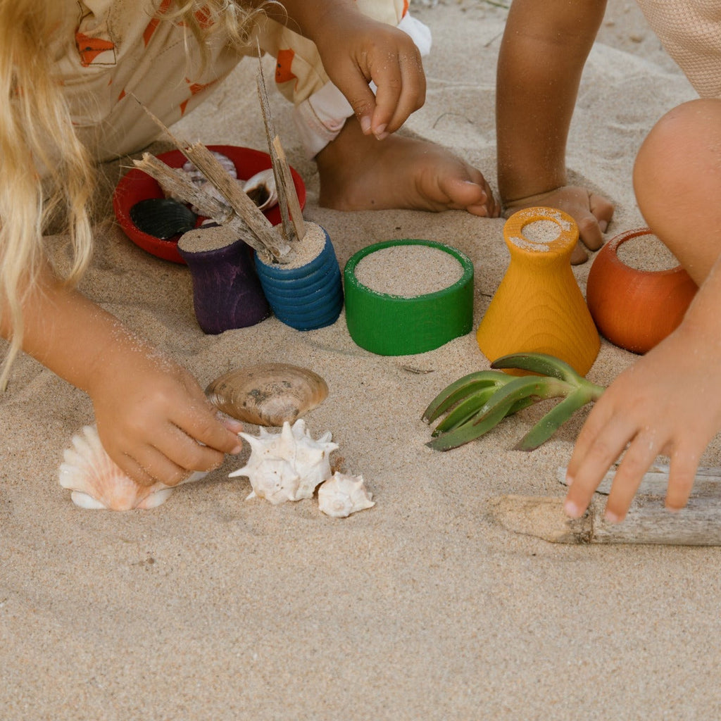 Children playing with grapat rainbow wooden pots at the beach 