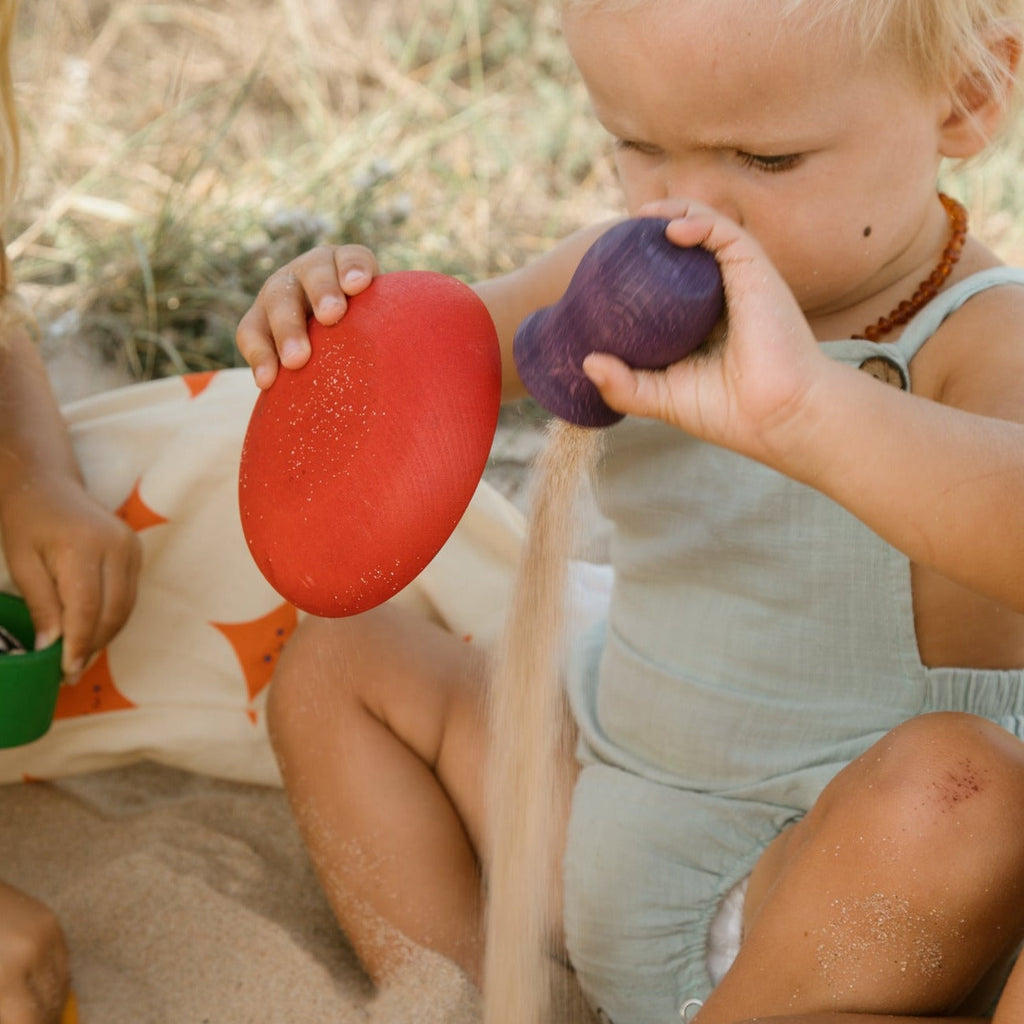 Child playing with rainbow wooden pots from Grapat 2024 release at the beach 