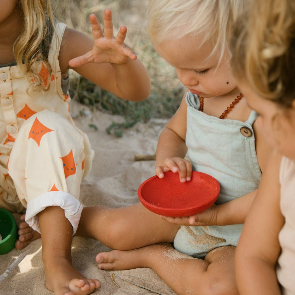 Child playing with red wooden dish from Grapat 2024 release at the beach 
