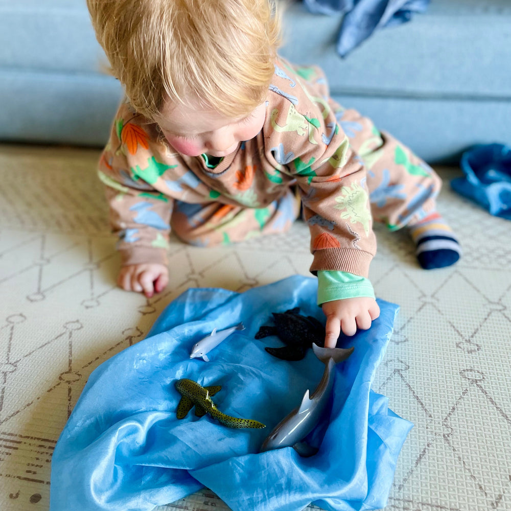 Child playing with ocean animals on play silk from monthly themed box