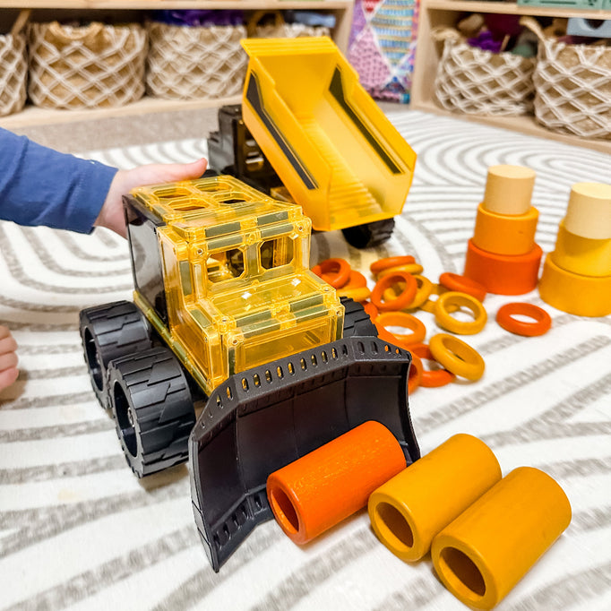 Toy bulldozer with attachments on a striped blanket in a playroom setting