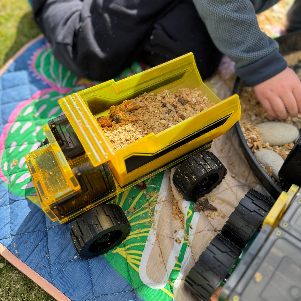 Toy dump truck on a colourful mat with children playing in the background