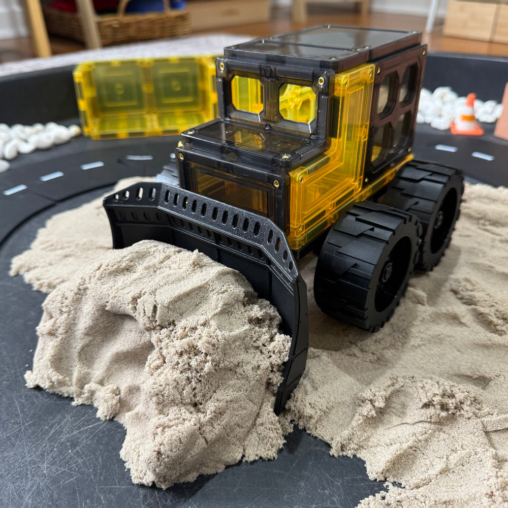 Toy bulldozer on a sand pit with a track layout in the background