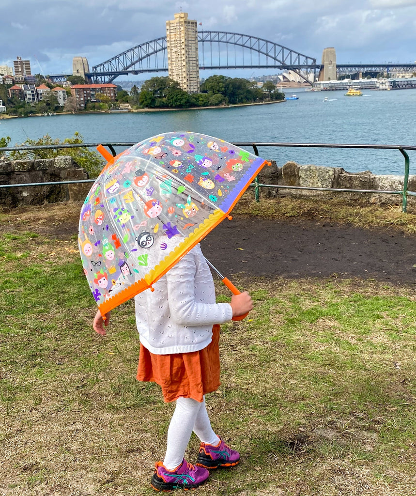 Djeco colour changing umbrella held by child looking across sydney harbour at the harbour bridge on a cloudy day