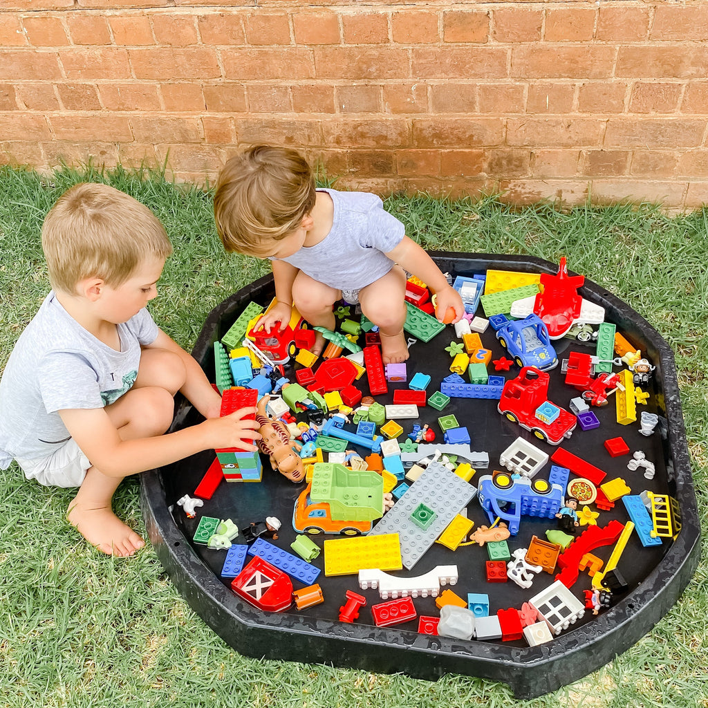Boys playing with tuff tray using it as lego storage tray outside 