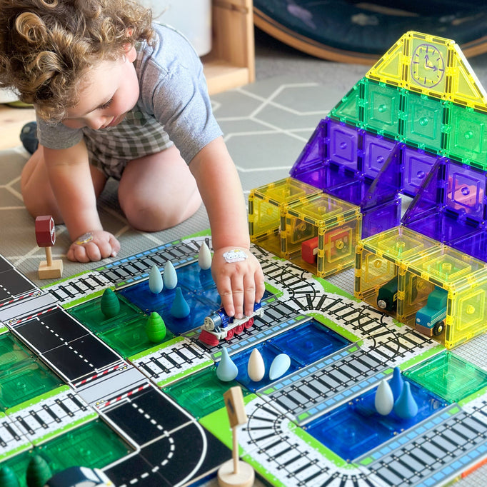 Child playing with train and road toppers that sit on magnetic tiles with train station made from learn and grow magnetic tiles 