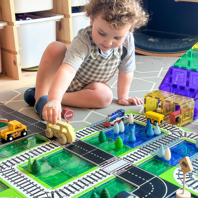 Child playing with train and road toppers that sit on magnetic tiles with train station made from learn and grow magnetic tiles