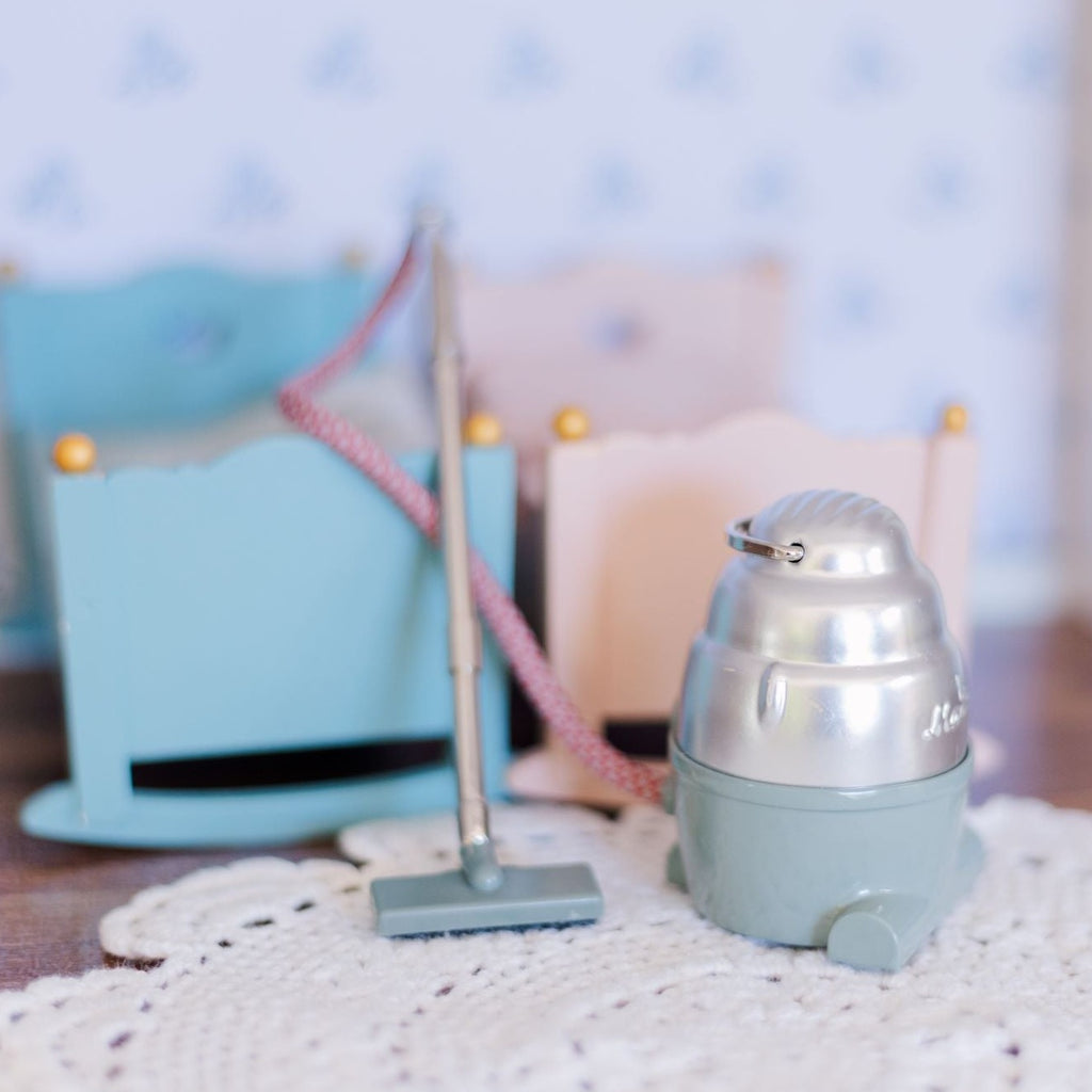Maileg Vacuum Cleaner sitting in dollhouse with blue and pink cradle in background