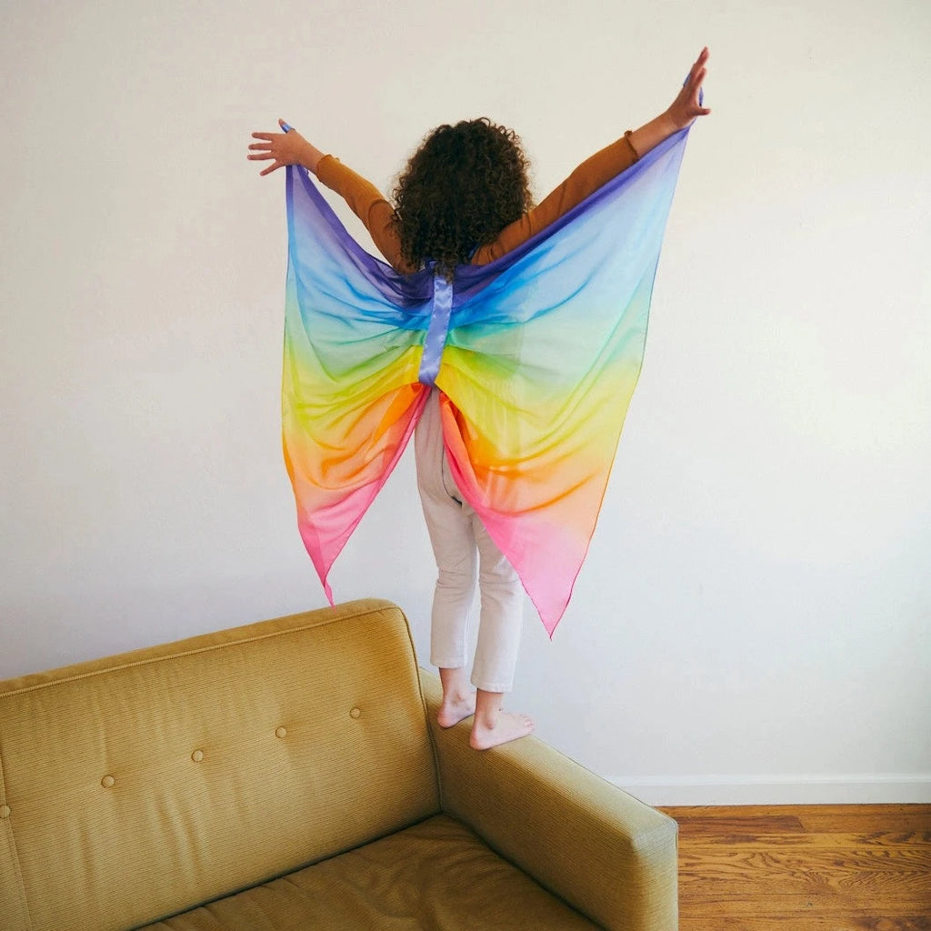 Child wearing rainbow fairy wings with amrs outstretched