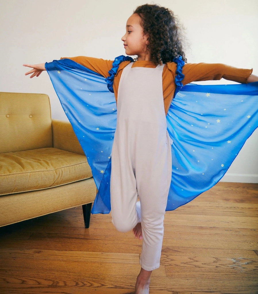 Child wearing starry night fairy wings with arms outstretched and standing on one leg