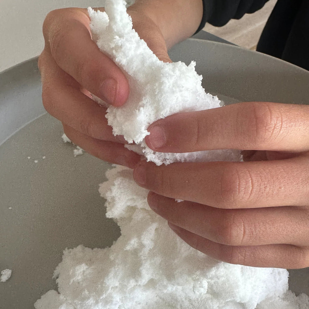 Hand holding a clump of white snow against a neutral background