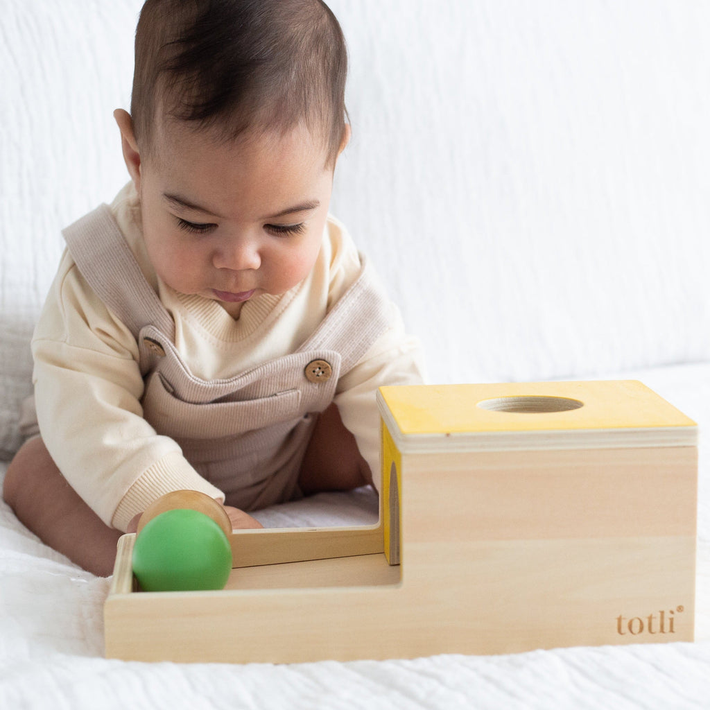 Toddler on bed looking at ball on The Totli Ball Drop a montessori inspired baby toy