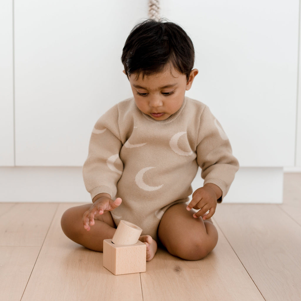 Child dressed in moon knitted onesie looking at pincer puzzle on floor