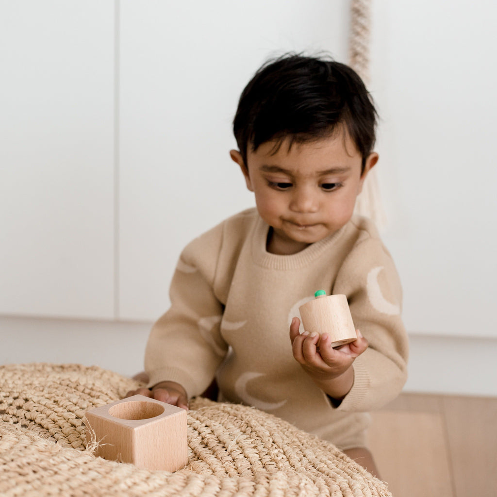 Child dressed in moon knitted onesie looking at pincer puzzle in his hand with a confused face