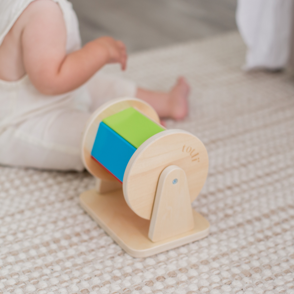 The Totli Spinning drum for babies displayed on rug with baby next to it