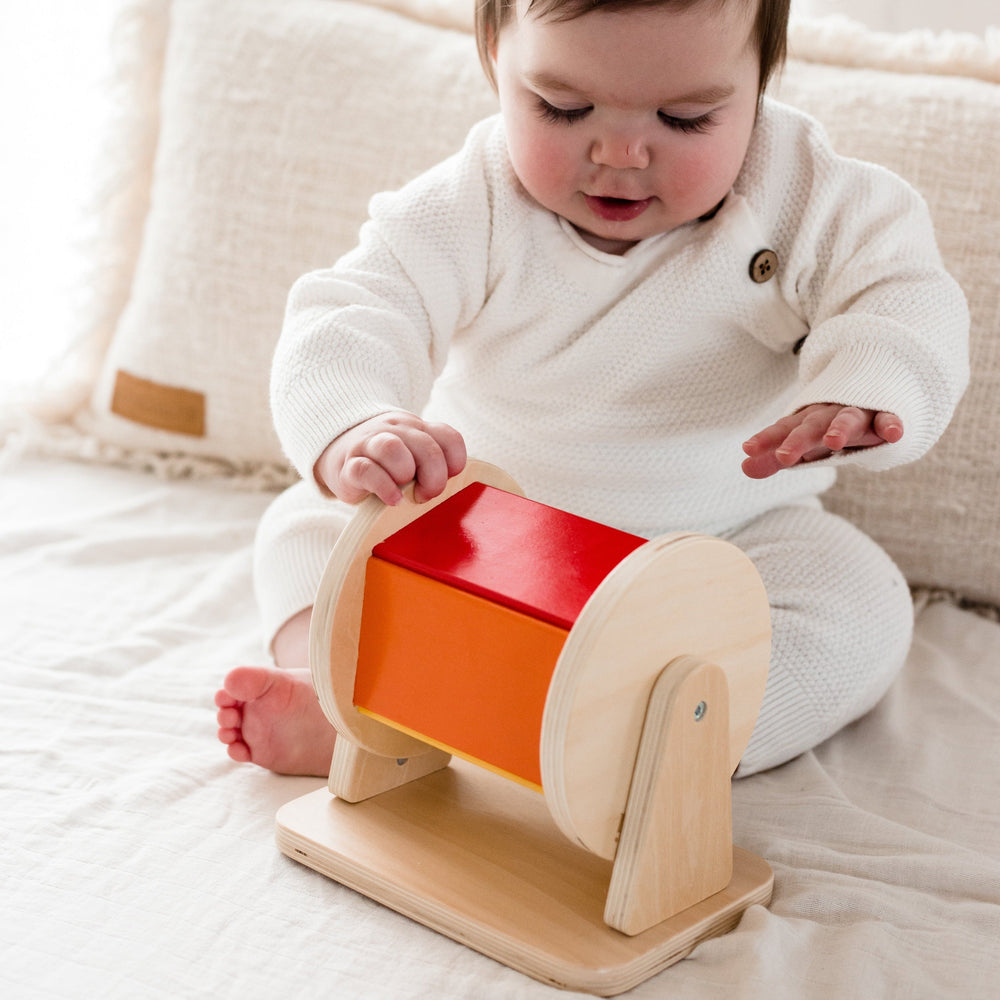 Baby in cream outfit on bed holding and playing with The Spinning Drum