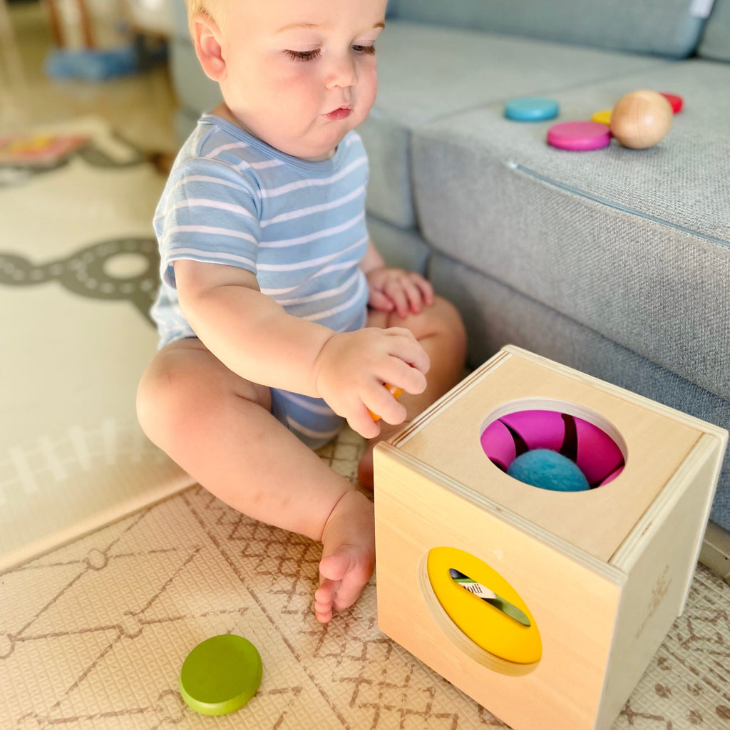 Baby playing with montessori Totli Box holding wooden disc in hand