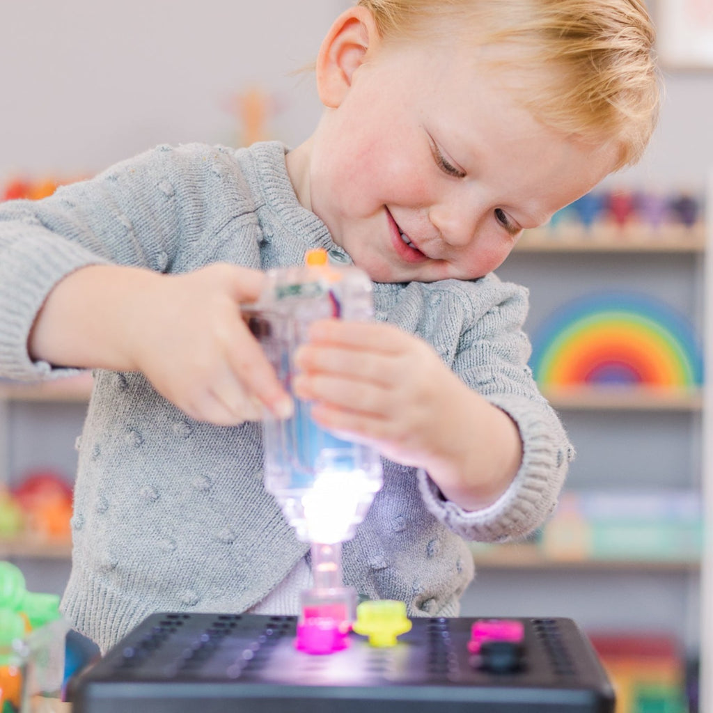Child dressed in grey jumper using light up drill in playroom
