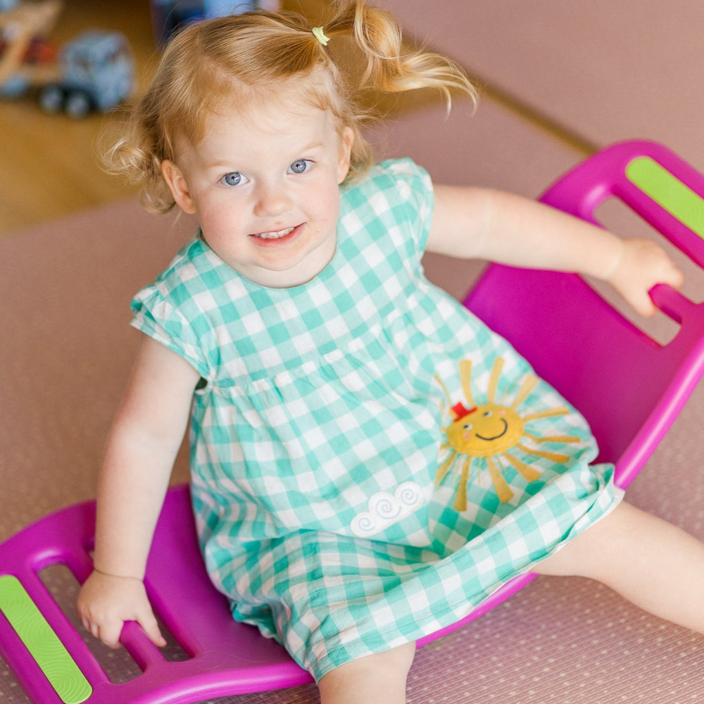  A girl sitting on a pink Fat Brain Toys - Teeter Popper balancing and holding on