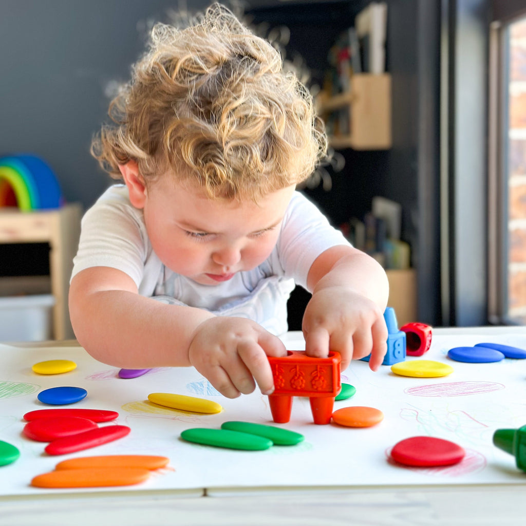 Child using crayons around rainbow junior pebbles