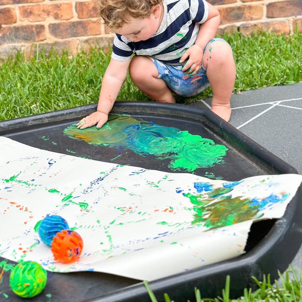 Child playing with sensory rollers and paint on a tuff tray