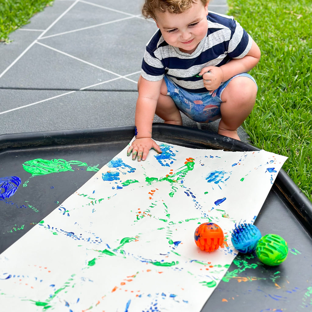 Child playing with sensory rollers and paint on a tuff tray