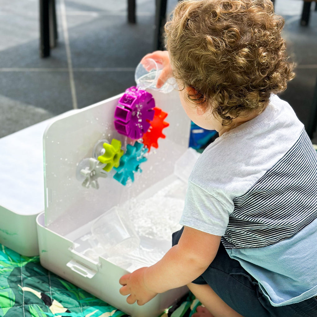 Child pouring water into cogs set up on tray lid