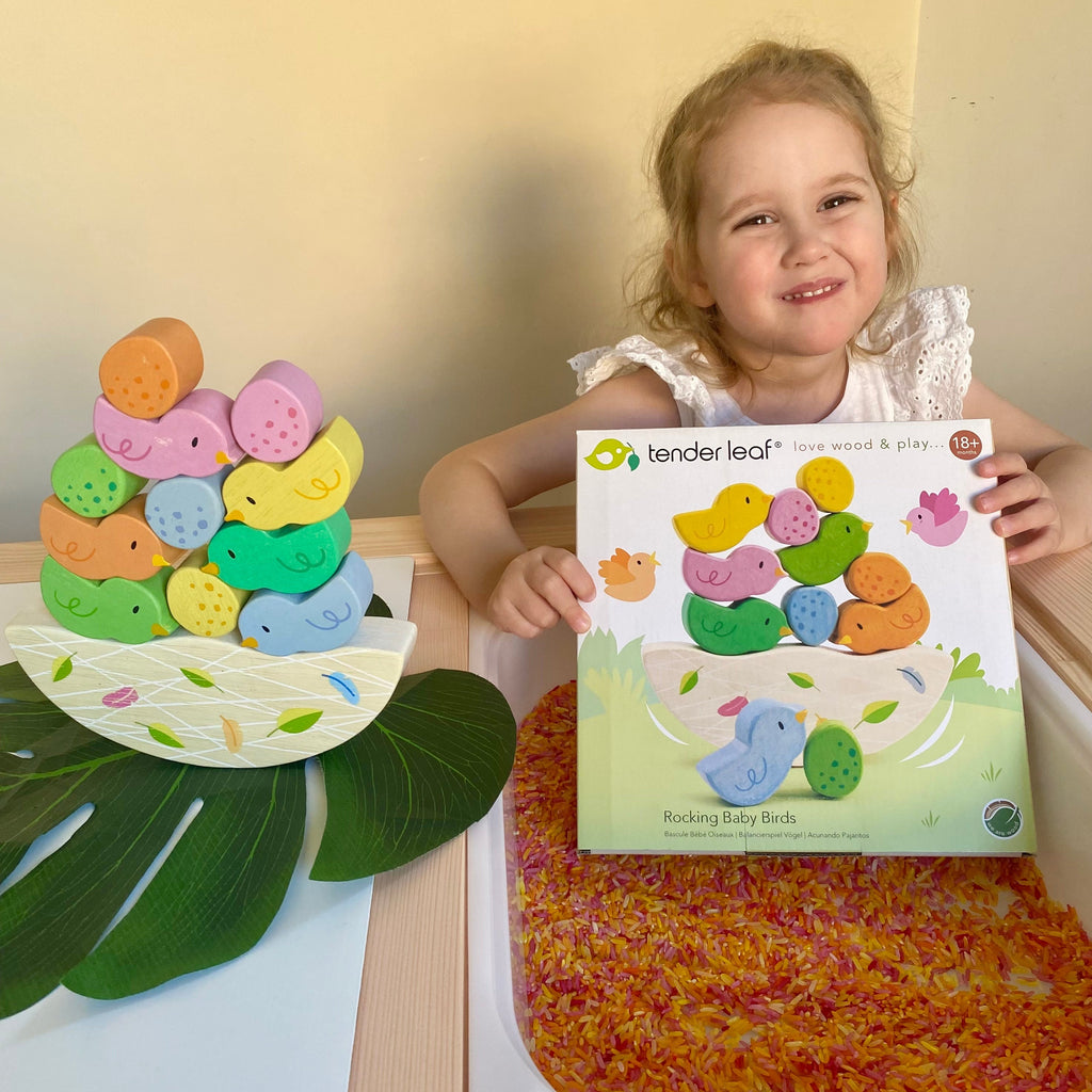 Child holding box of rocking baby birds wooden puzzle with sensory rice in a flisat table
