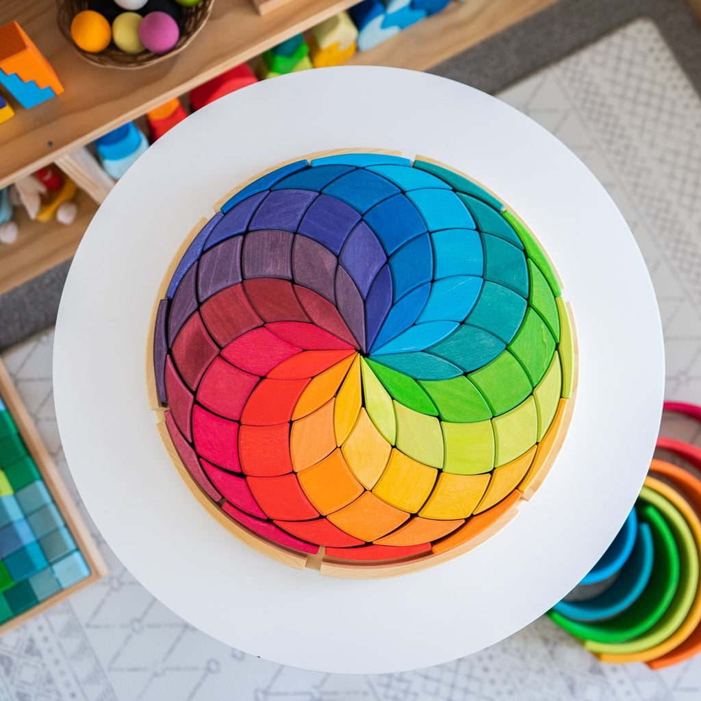 Grimm's large mandala circle coloured spiral sitting on a white table in a playroom with grimm's toys in background