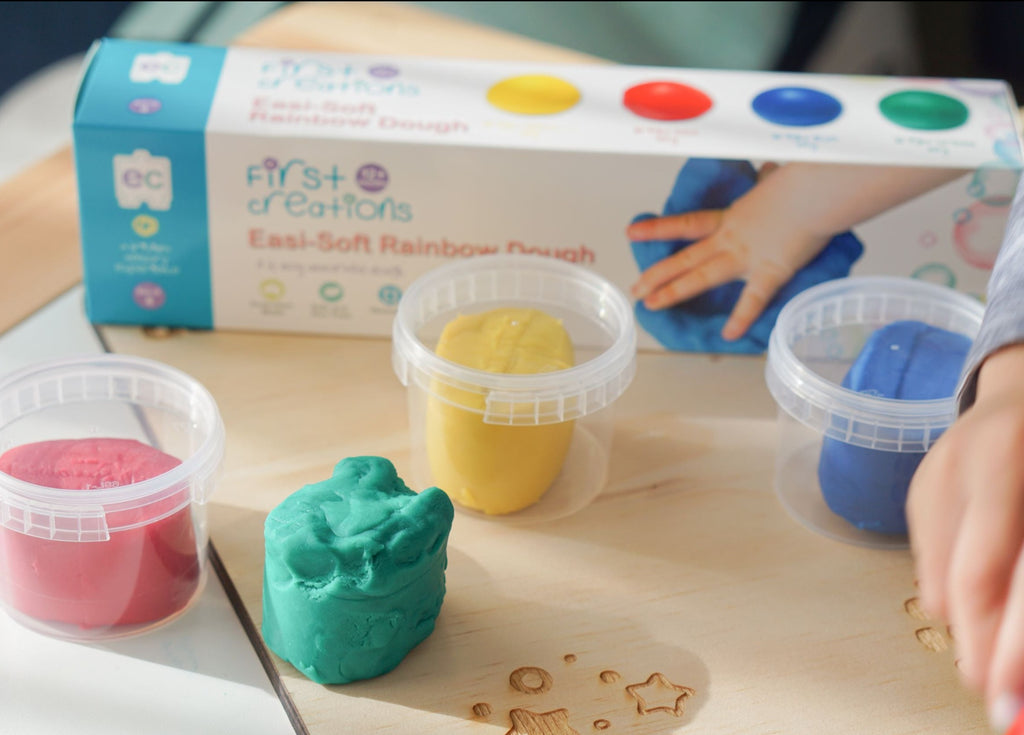 Easi-Soft Rainbow Dough with four plastic pots of coloured dough shown on wooden mat