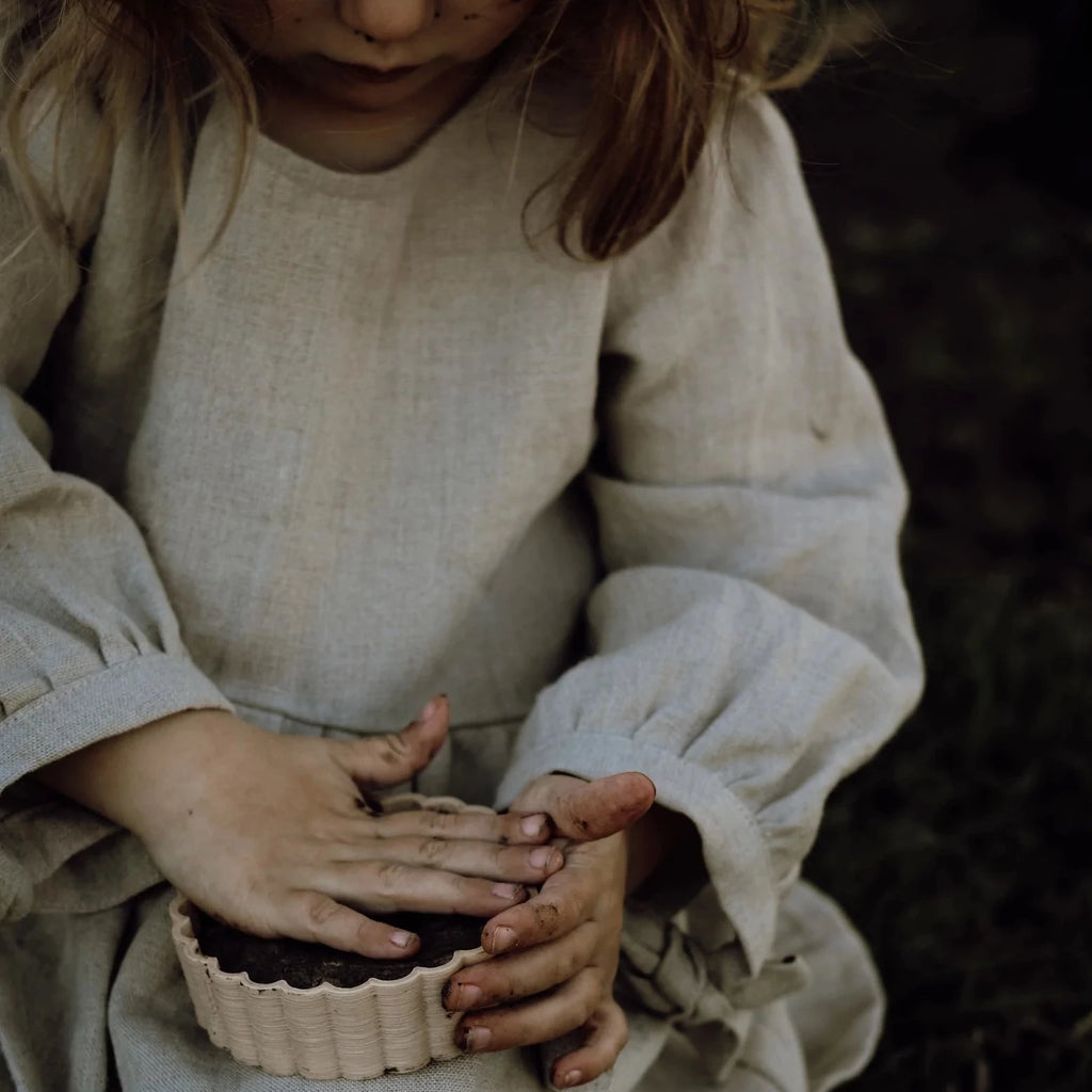 Girl in beige linen dress playing with mud pie mould from Kinfolk & CO