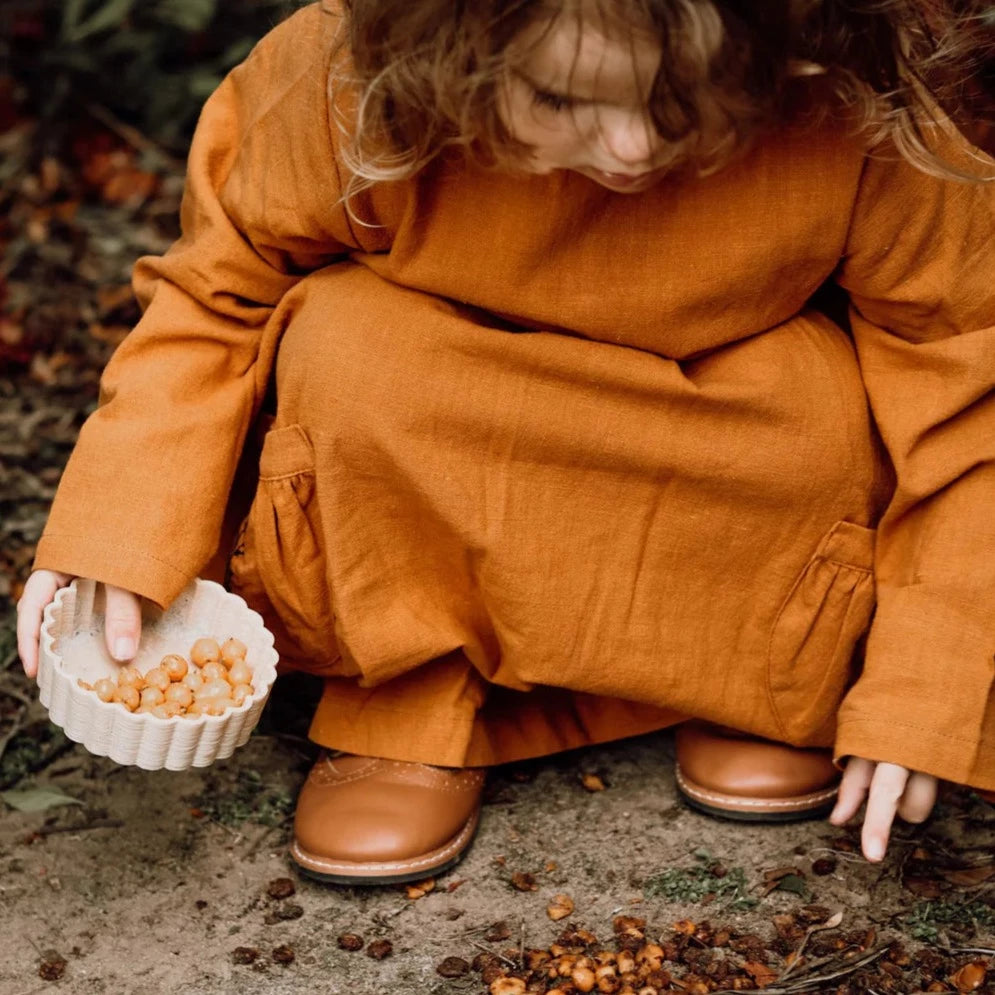 Girl in orange linen dress playing with mud pie mould from Kinfolk & CO