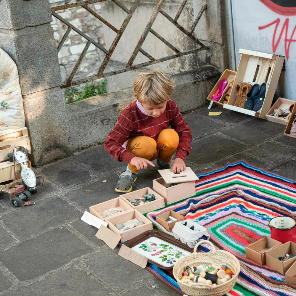 Child playing with Grapat Permanence Box sitting on a colourful rug in a city street