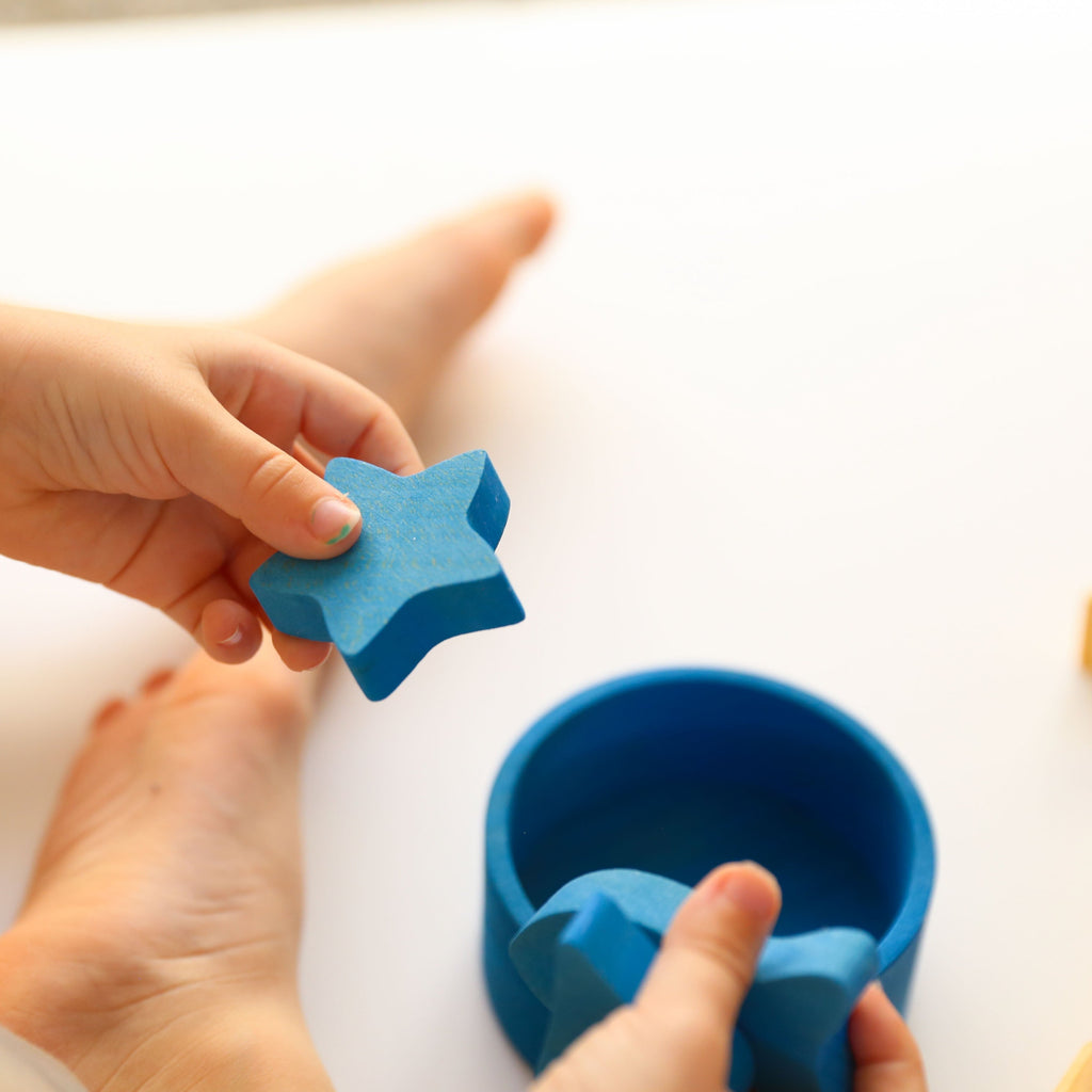 Blue wooden star in Grimm's rainbow sorting game being held by a toddler