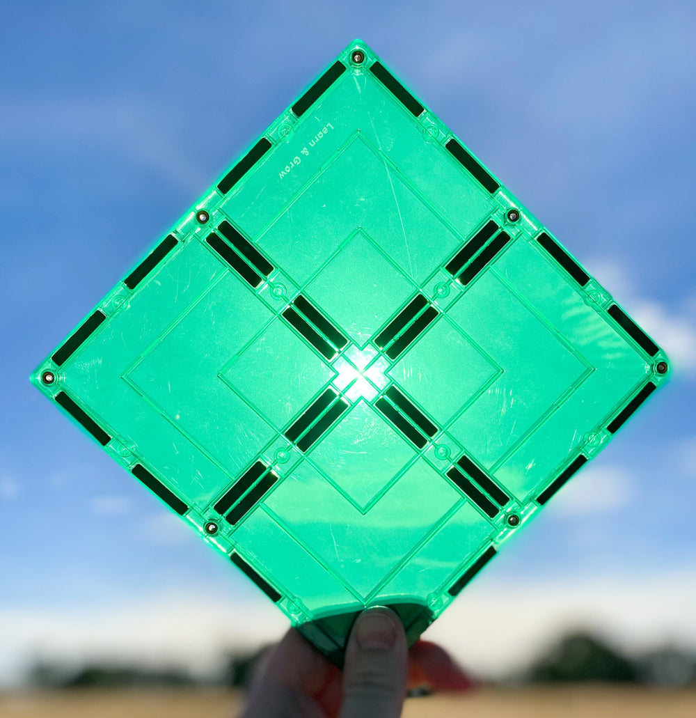Large green magnetic square tile held up against sun and blue skies