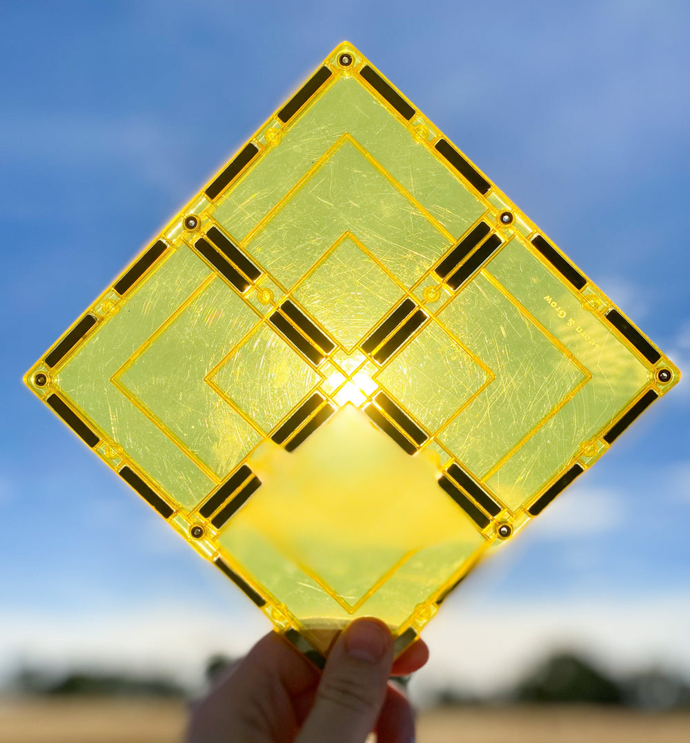 Large yellow magnetic square tile held up against sun and blue skies