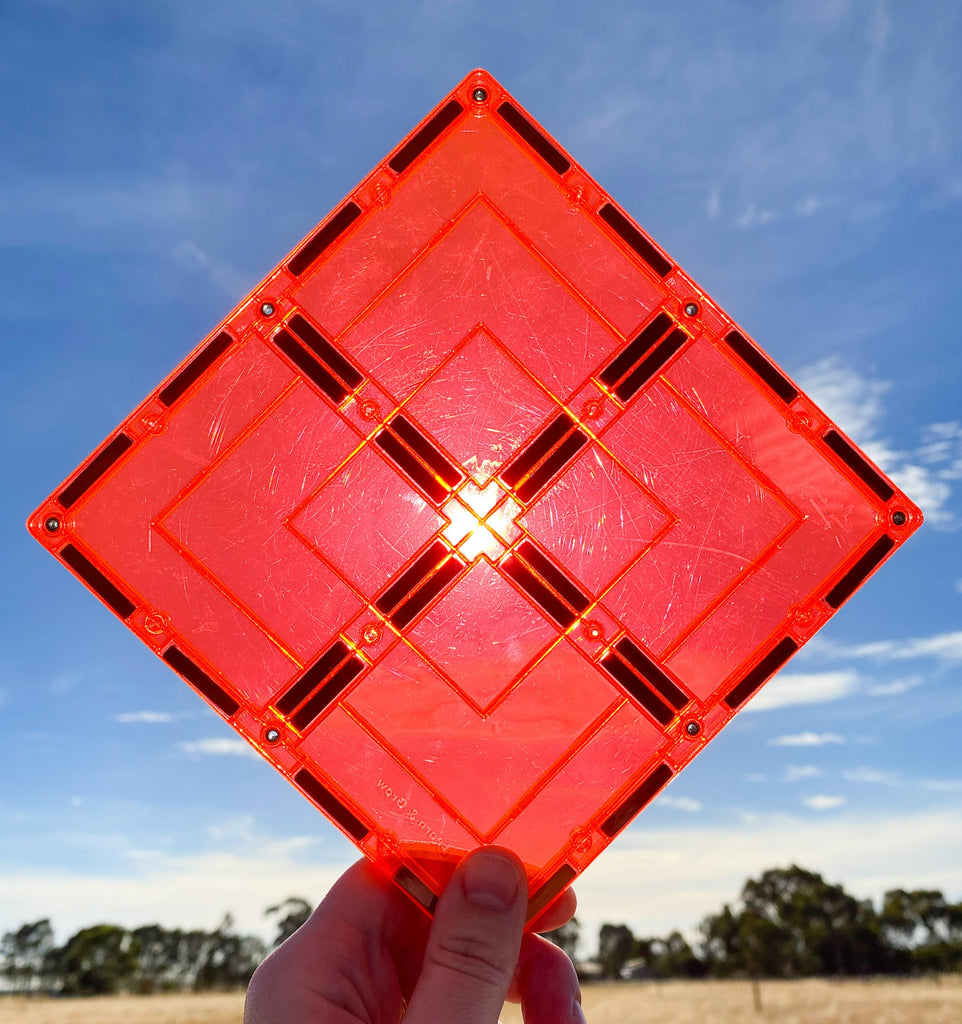 Large red magnetic square tile held up against sun and blue skies