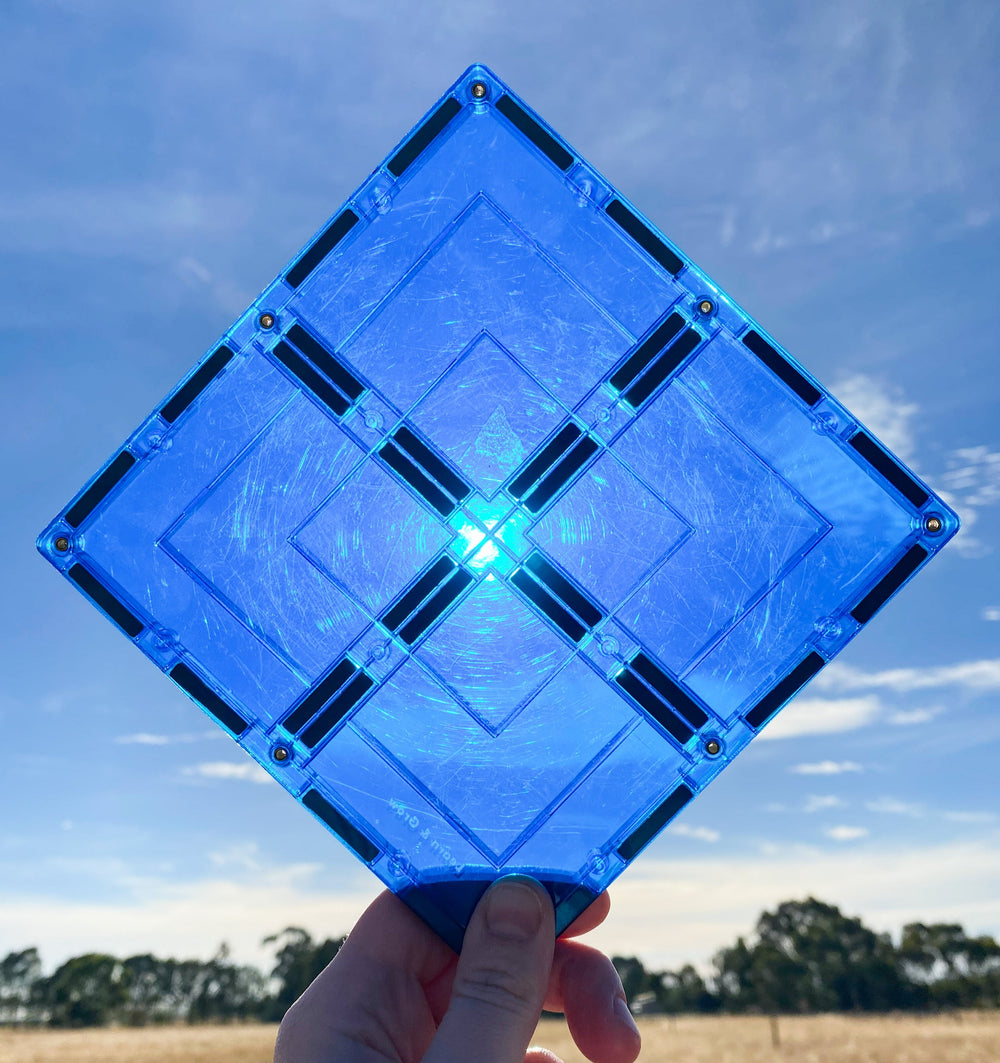 Large blue  magnetic square tile held up against sun and blue skies